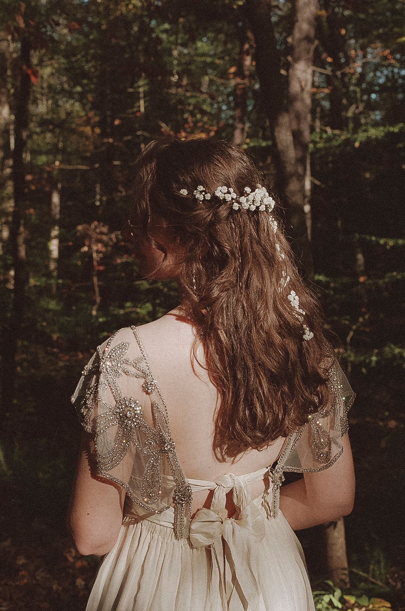 Back view of vintage-style cream wedding dress with delicate lace details and bow in a forest setting.