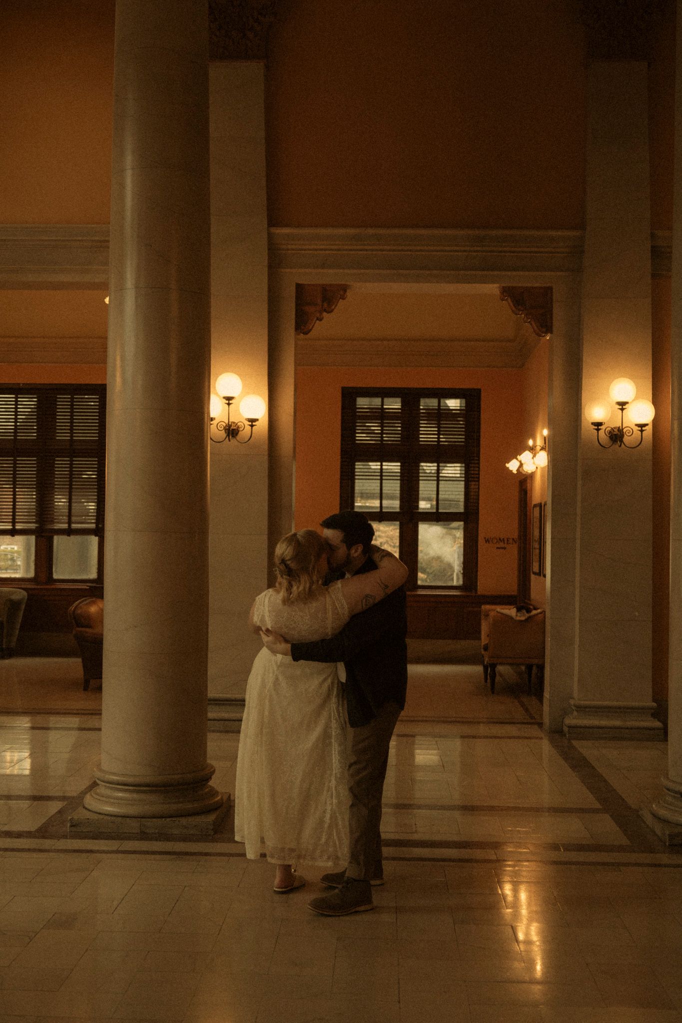 A couple dances in a grand hallway with marble columns and warm lighting creating a romantic atmosphere.
