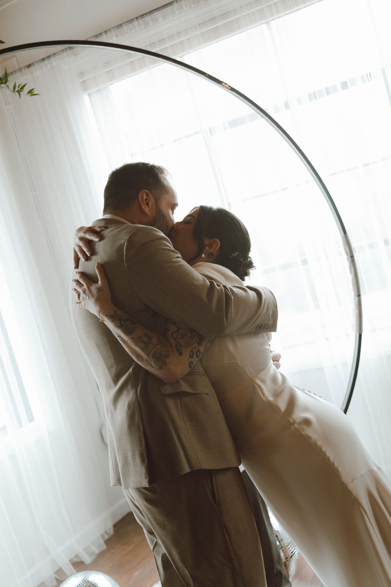 Two people embrace in an intimate moment against a bright white background with a curved architectural element.