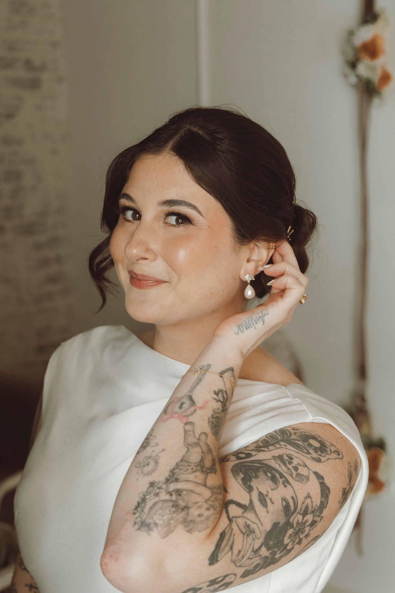 Bride with elegant updo and tattoos putting on earrings while getting ready.