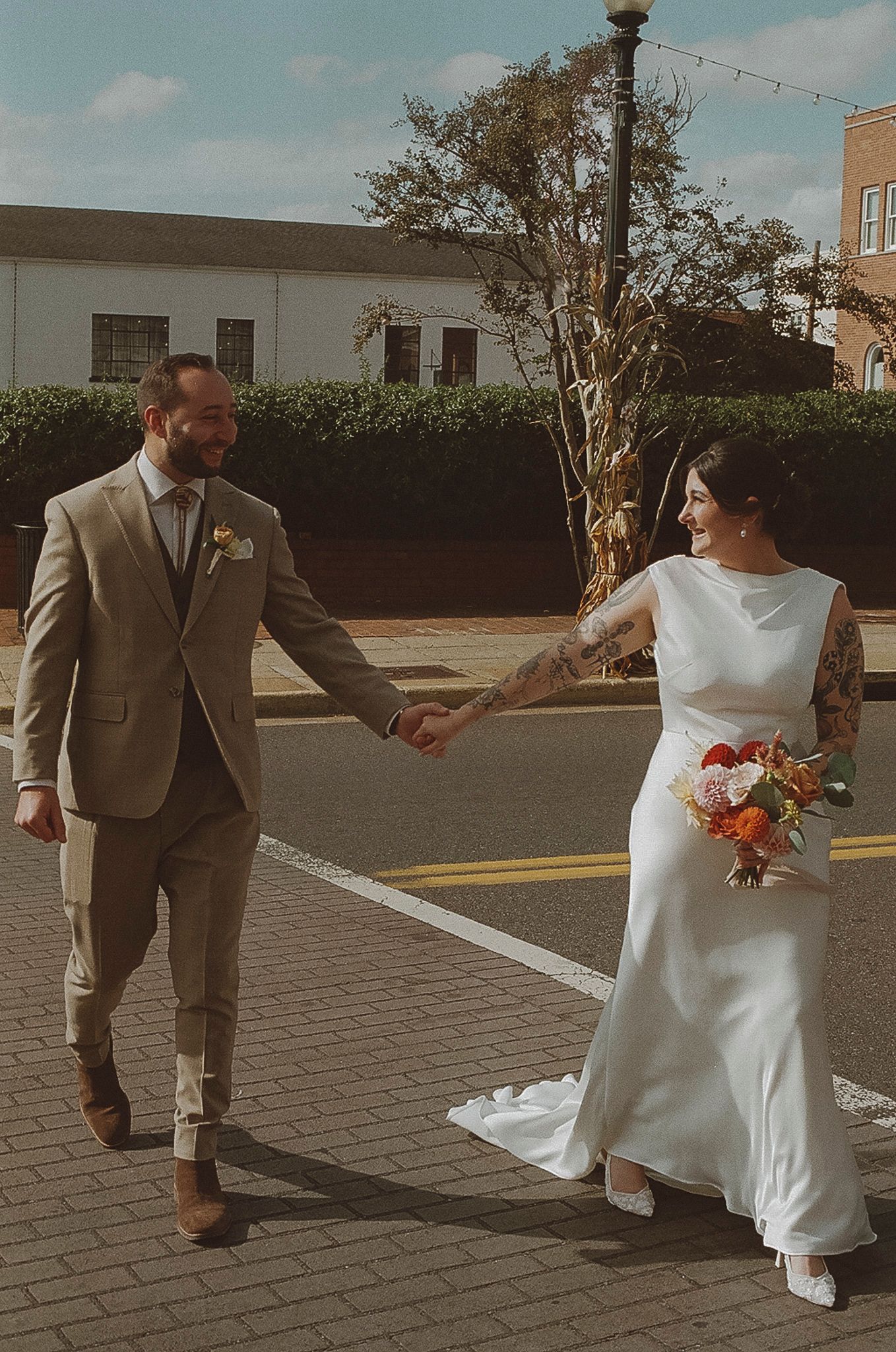 A couple in wedding attire holds hands while walking across a brick paved area.