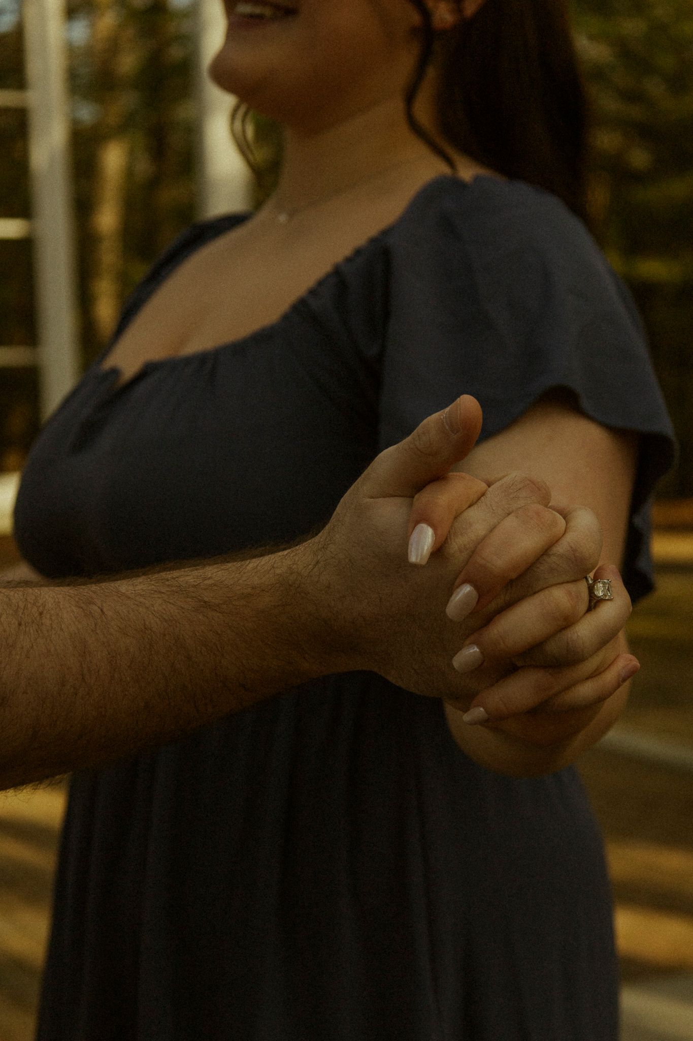 Close-up of a couple holding hands, woman wearing a navy dress and ring with white manicured nails.