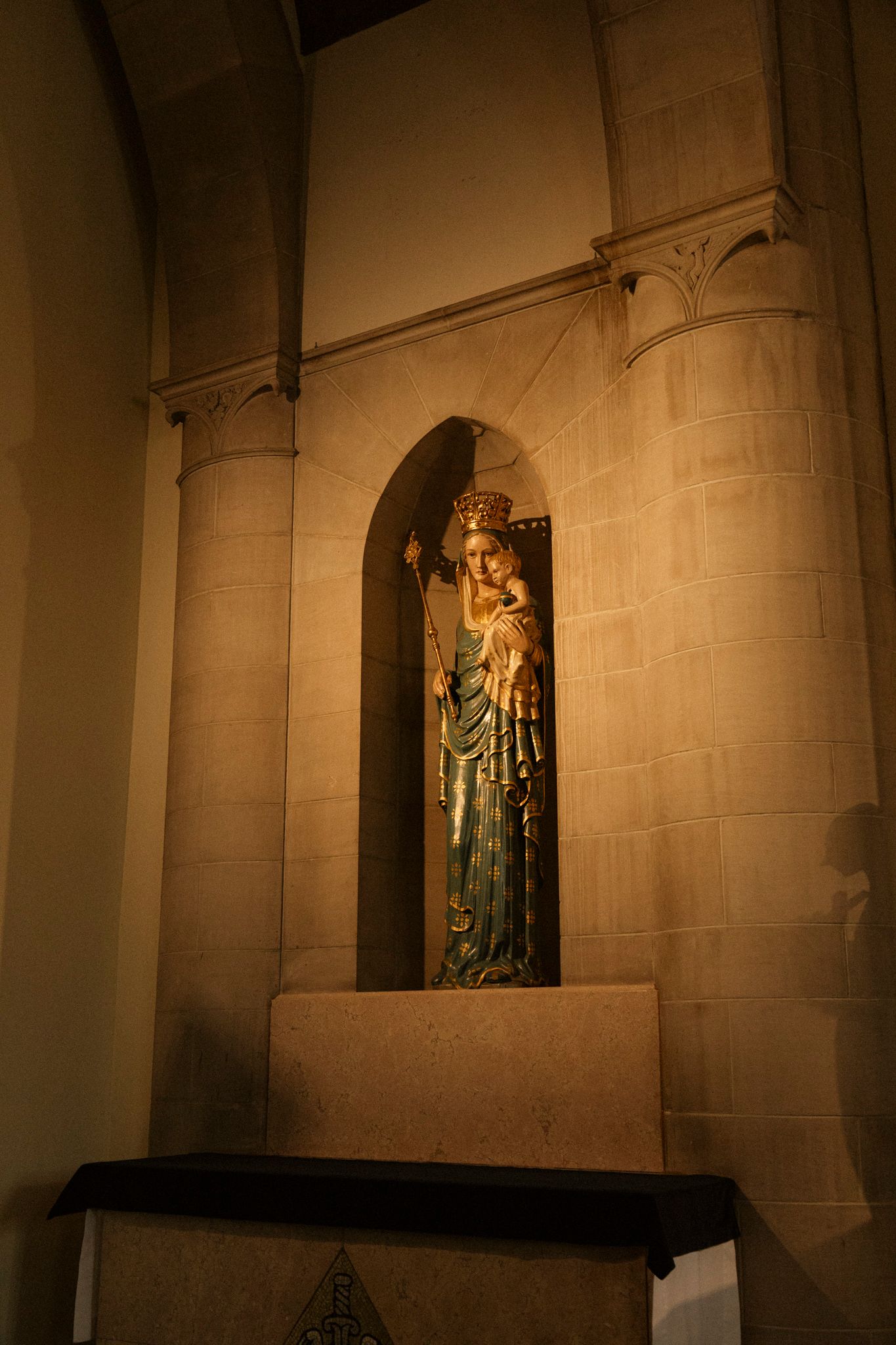 Golden Madonna and Child statue in an illuminated stone niche inside a historic Catholic church.