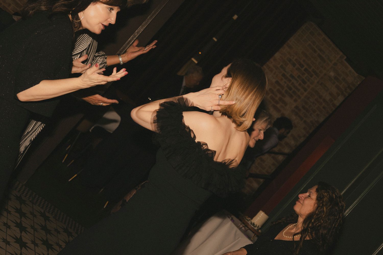 Wedding guests dancing energetically in darkened reception venue with dramatic lighting.