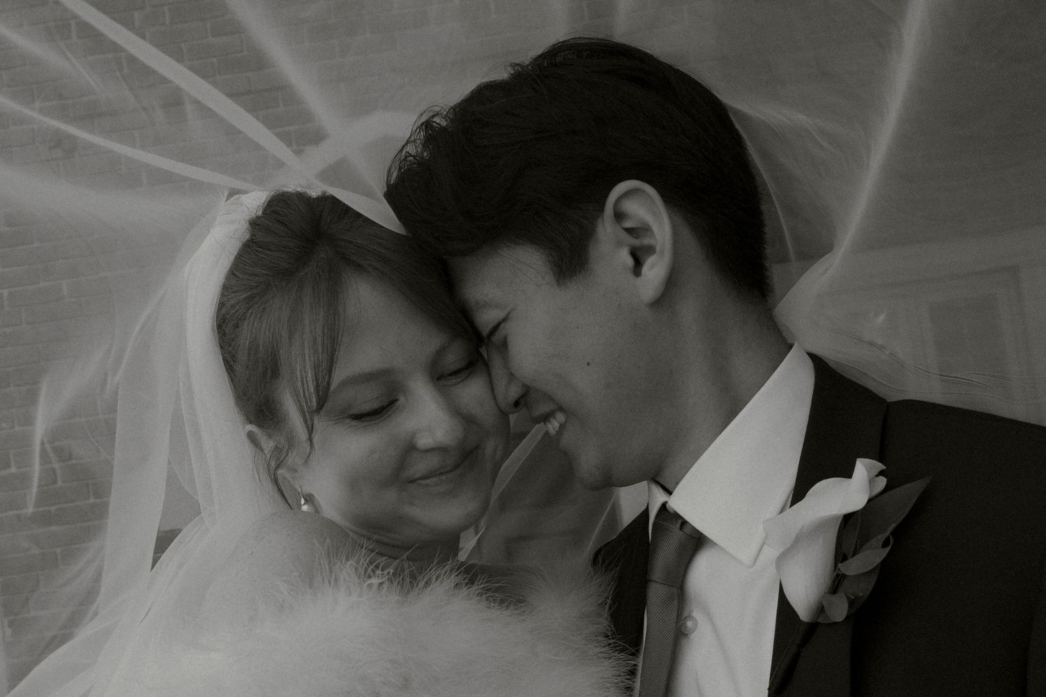 Black and white close-up of smiling bride and groom sharing a tender moment beneath a veil.