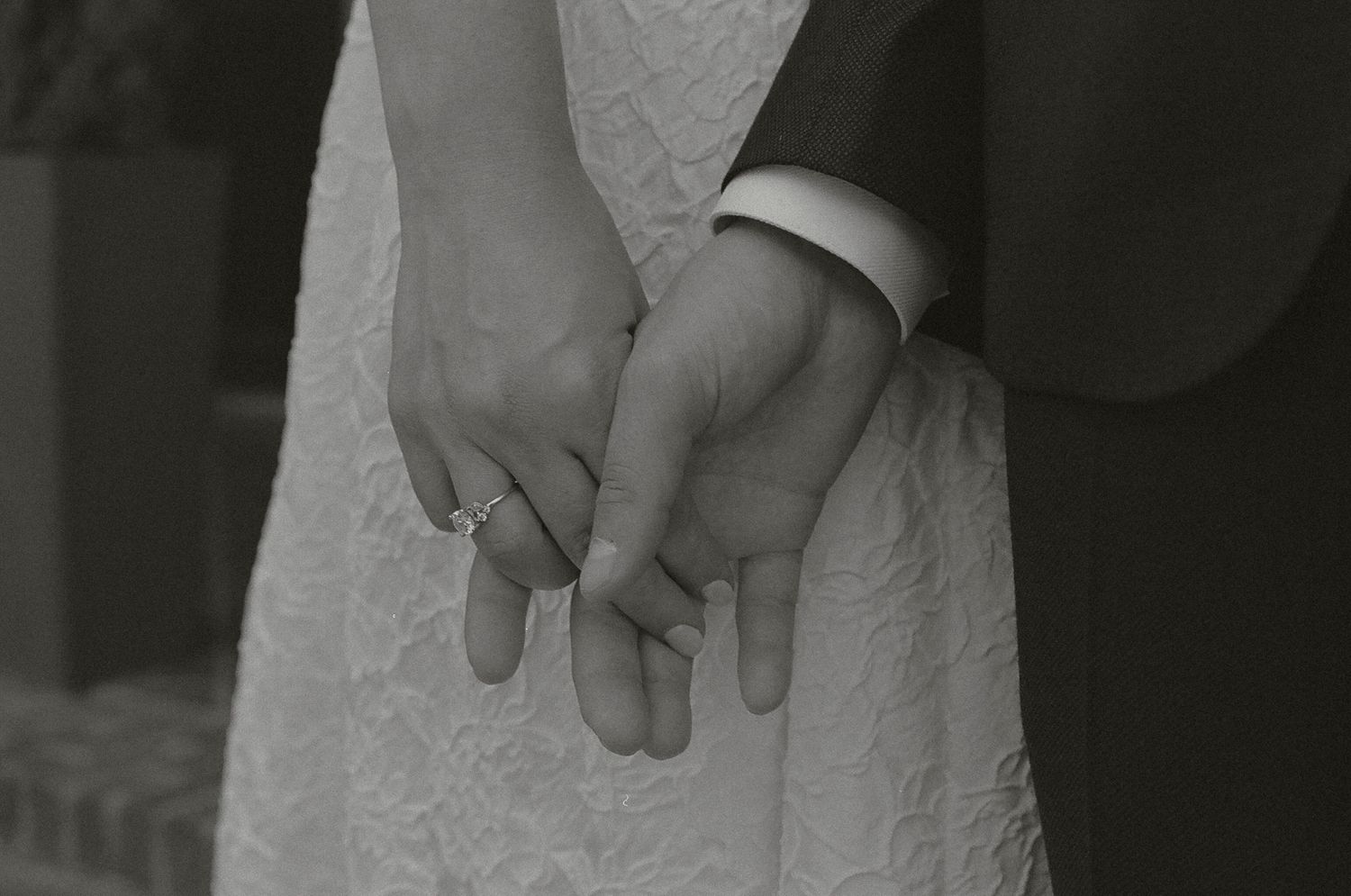 A close-up black and white photo shows hands holding and adjusting a delicate lace wedding dress detail.