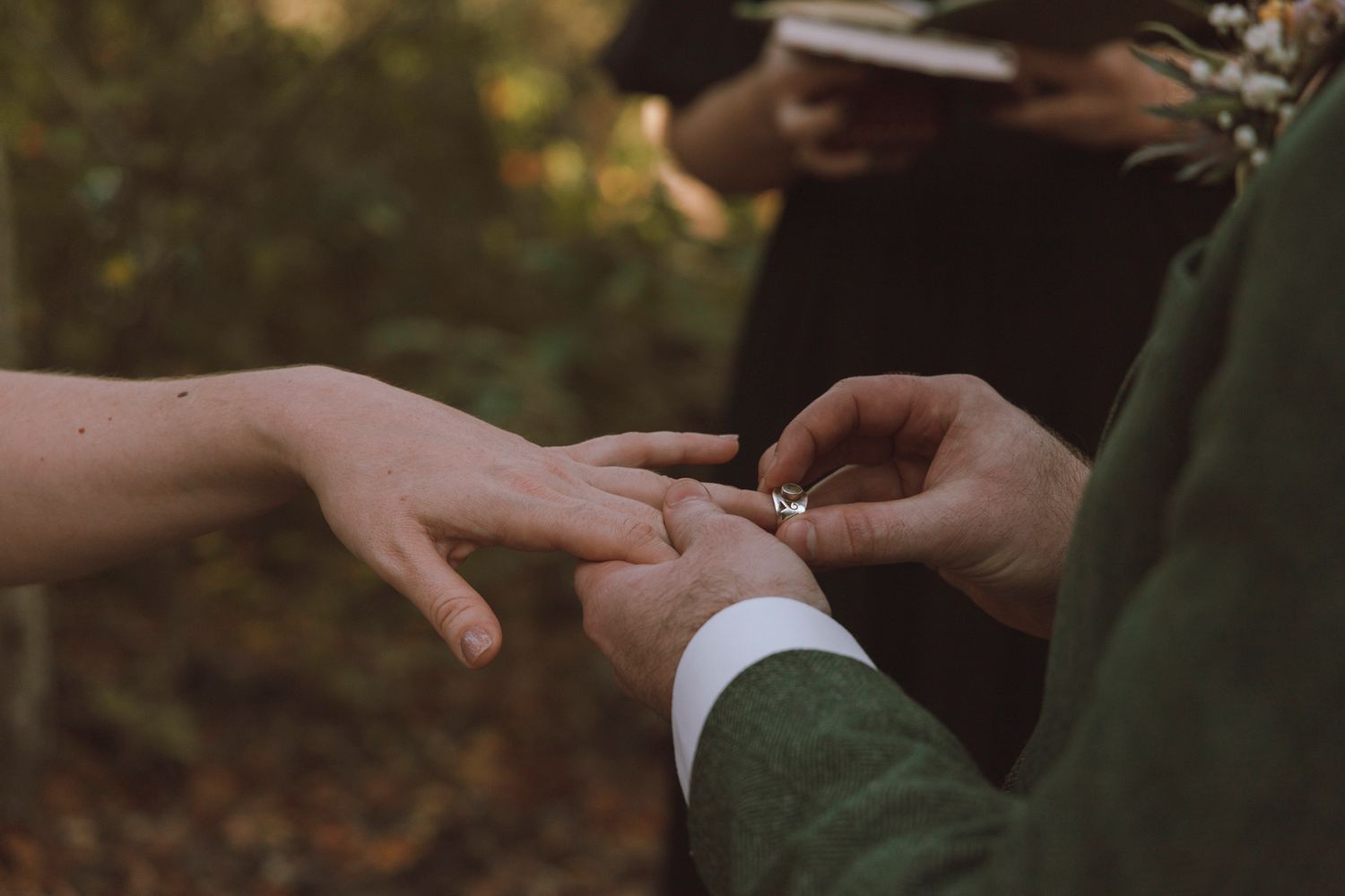 Close-up shot of hands exchanging wedding rings during an outdoor ceremony in natural lighting.