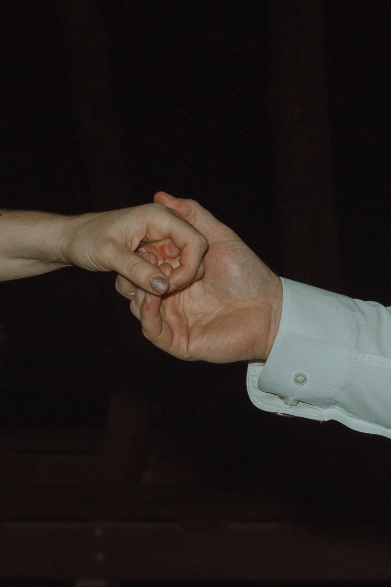 A sequence of hands in white sleeves performing a magic trick with a small object against a dark background.