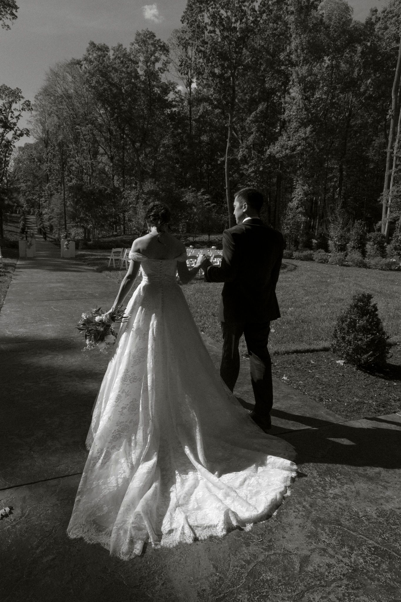 Black and white photo of a couple walking outdoors with a flowing wedding dress train.