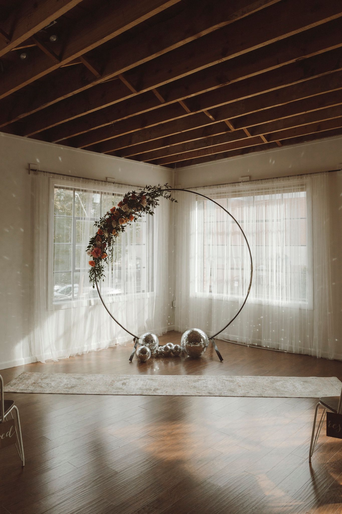 Large bright studio space with exposed wooden beams and sheer white curtains featuring circular floral installations.