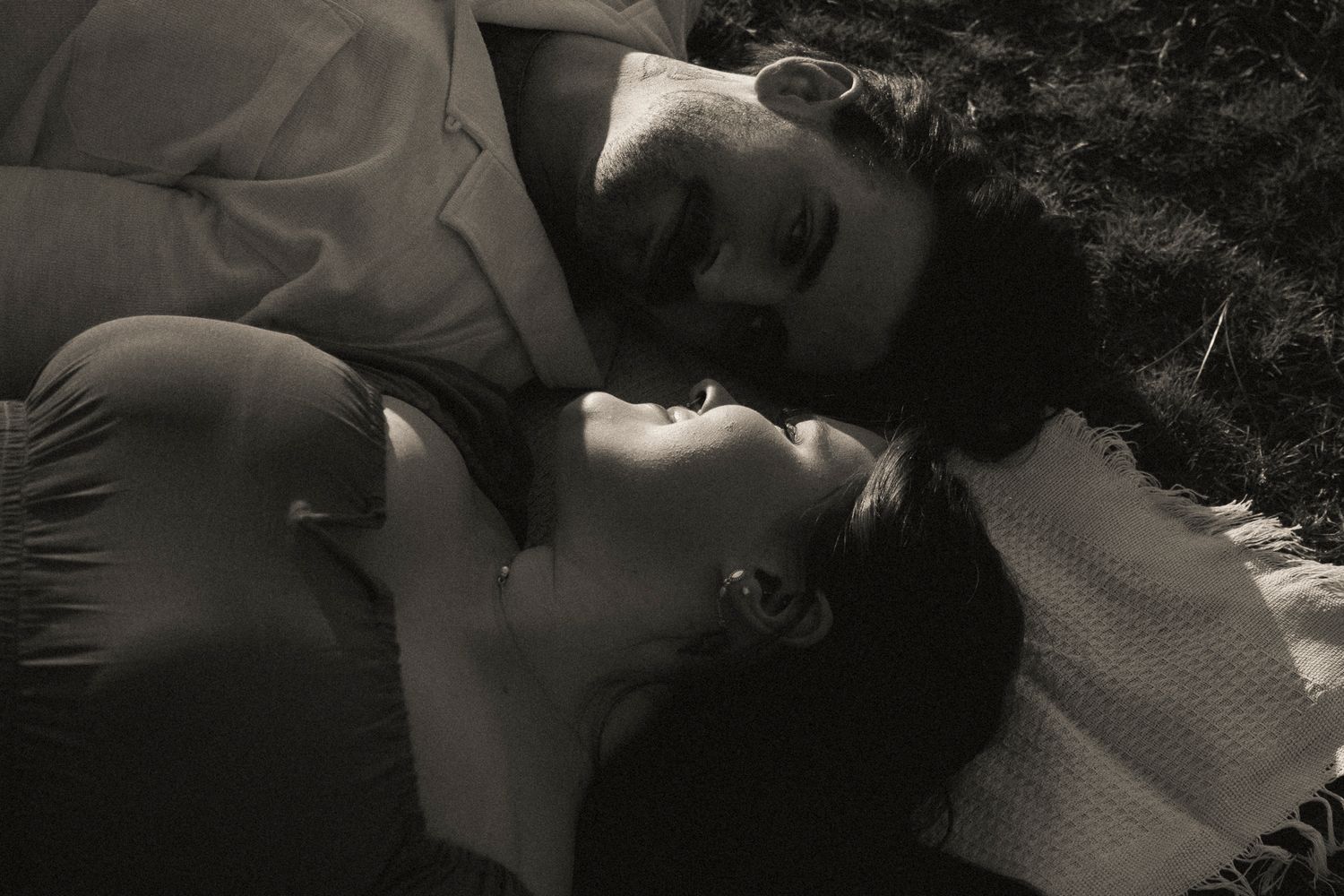Romantic black and white photo of a couple lying together on a blanket outdoors, gazing at each other.