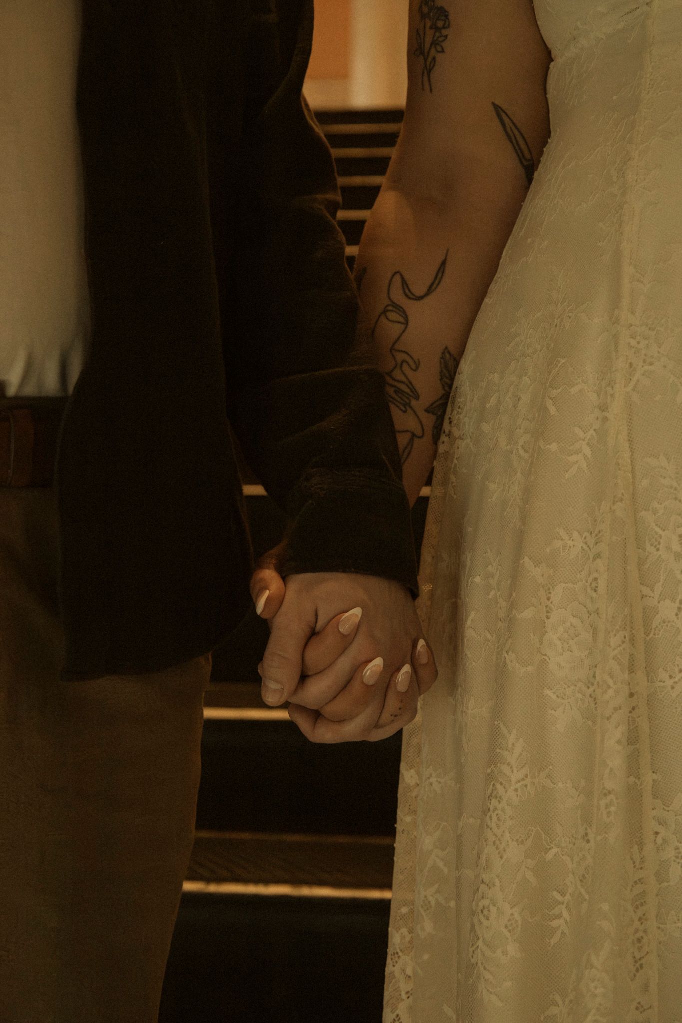 A couple holds hands during a wedding ceremony, with the bride in white and groom in dark formal attire.