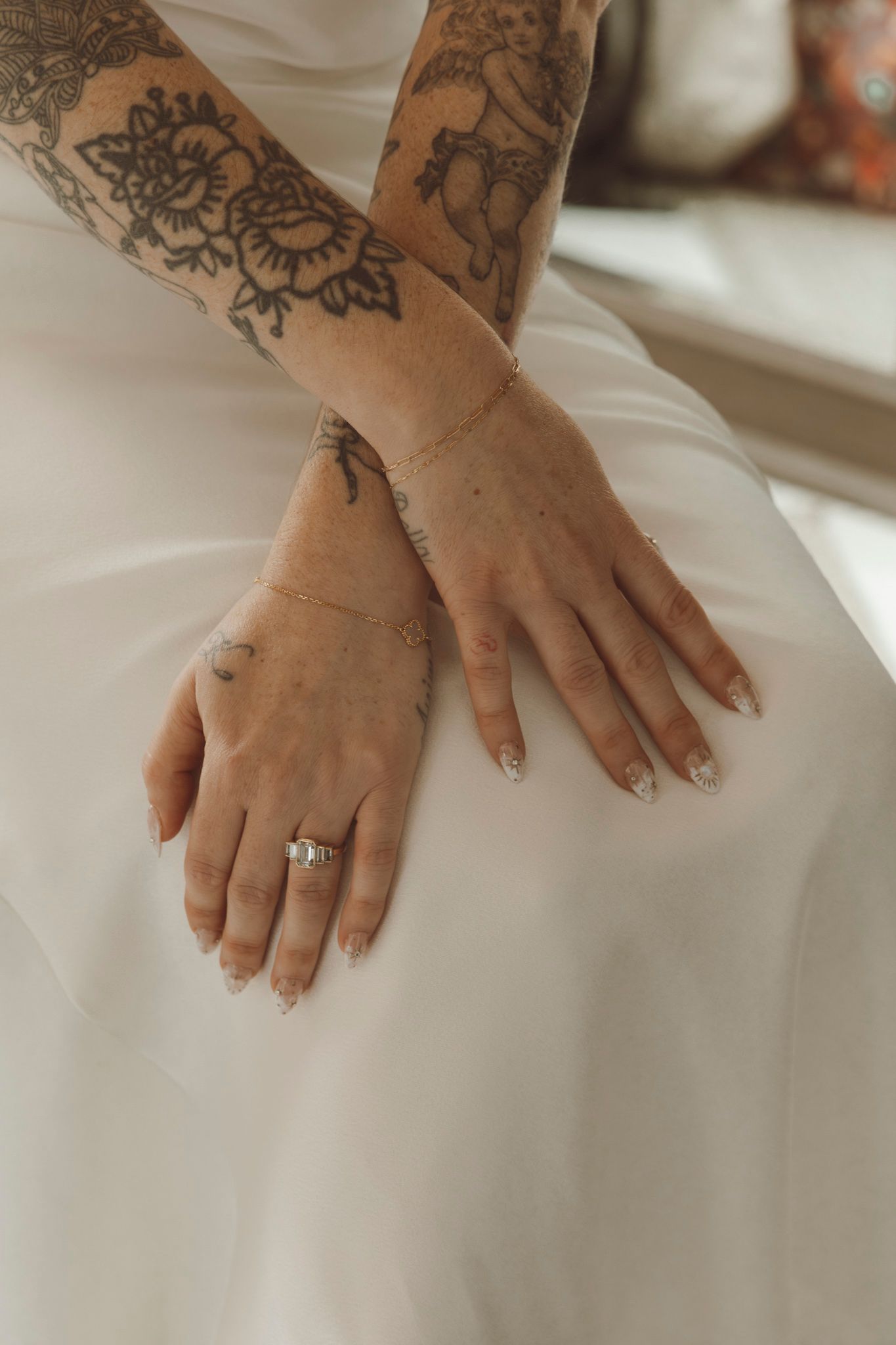 Close-up of hands with intricate floral tattoos and an engagement ring against a white dress.