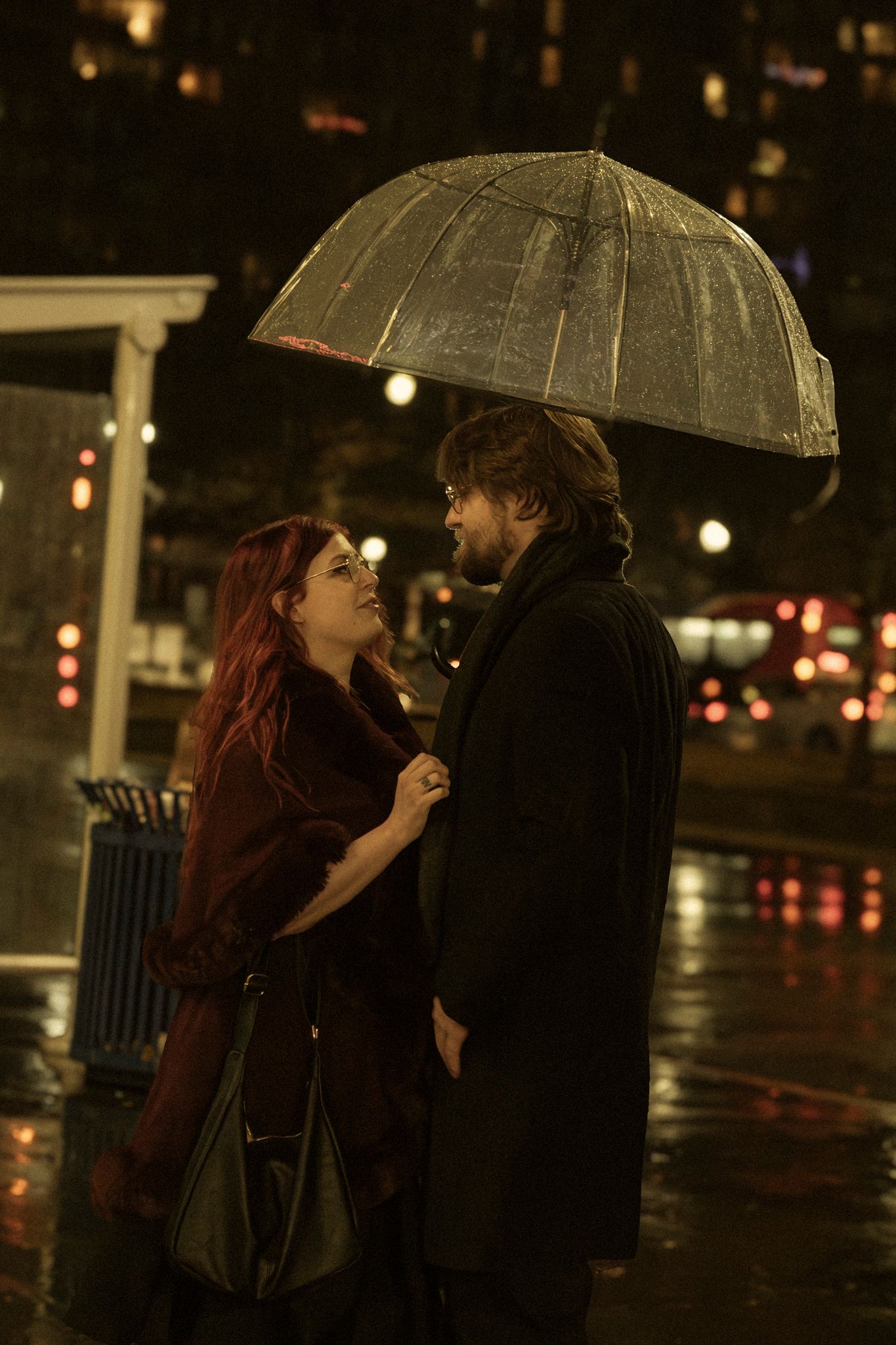 Two people sharing an umbrella while standing close together on a rainy city street at night.