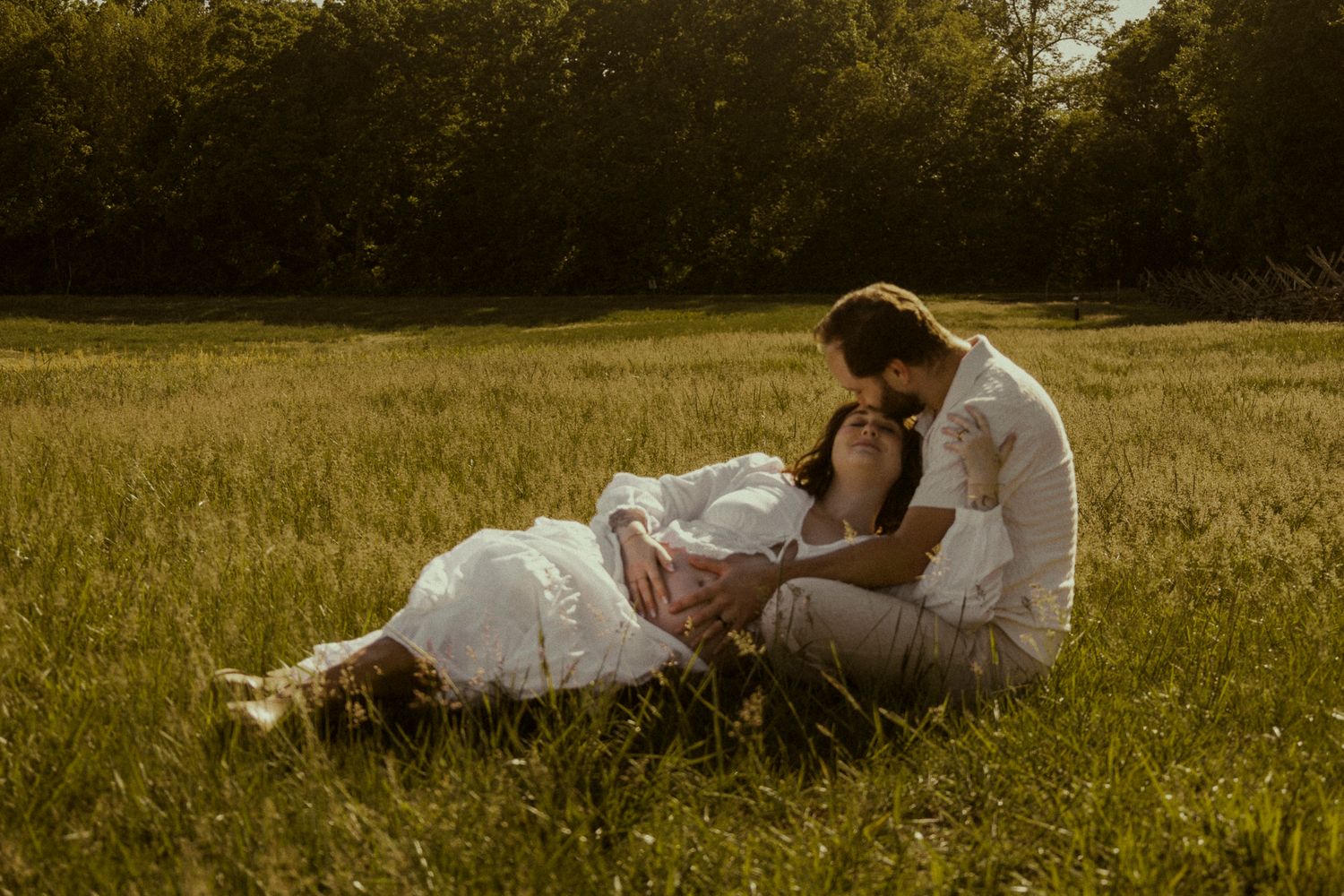Couple sharing a romantic moment in a sunlit green meadow, woman lying in mans arms during golden hour.