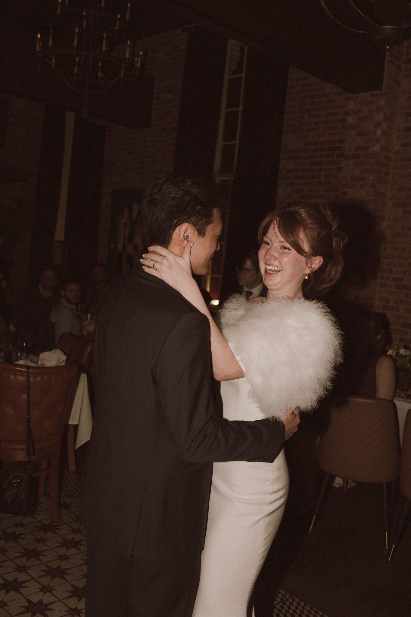 Bride in white gown with fur stole shares first dance with groom at wedding reception.