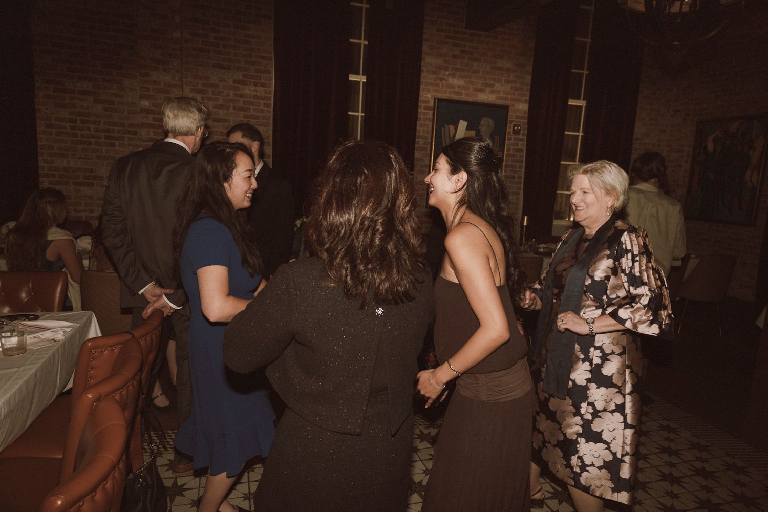 Wedding reception guests mingling and dancing in warmly lit brick-walled venue.