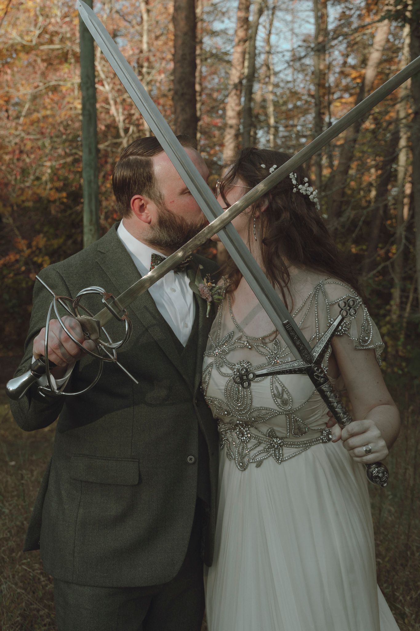 A romantic autumn forest wedding scene with a couple in formal attire holding crossed swords during their ceremony.