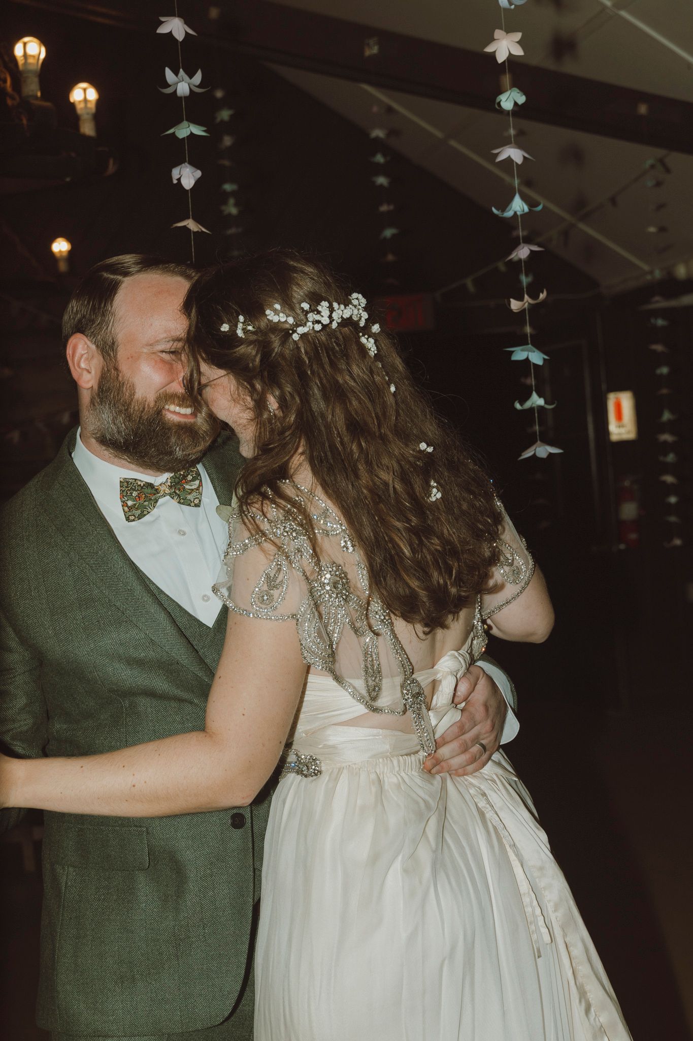 A couple shares an intimate dance moment at a reception under hanging paper decorations.