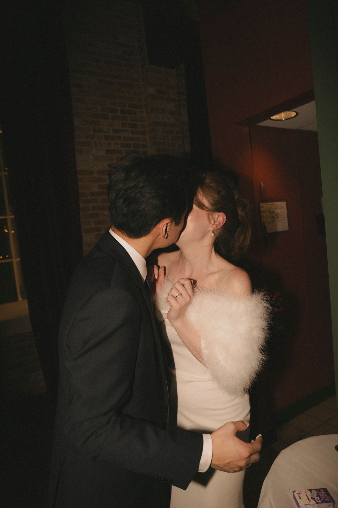 Bride in white dress with fur stole shares romantic kiss with groom at wedding reception.