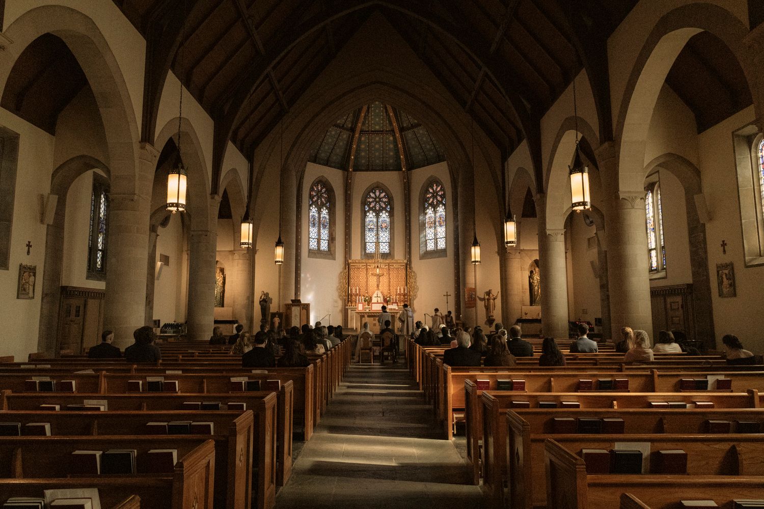 Wide angle view of elegant church interior with wooden pews and ornate altar.