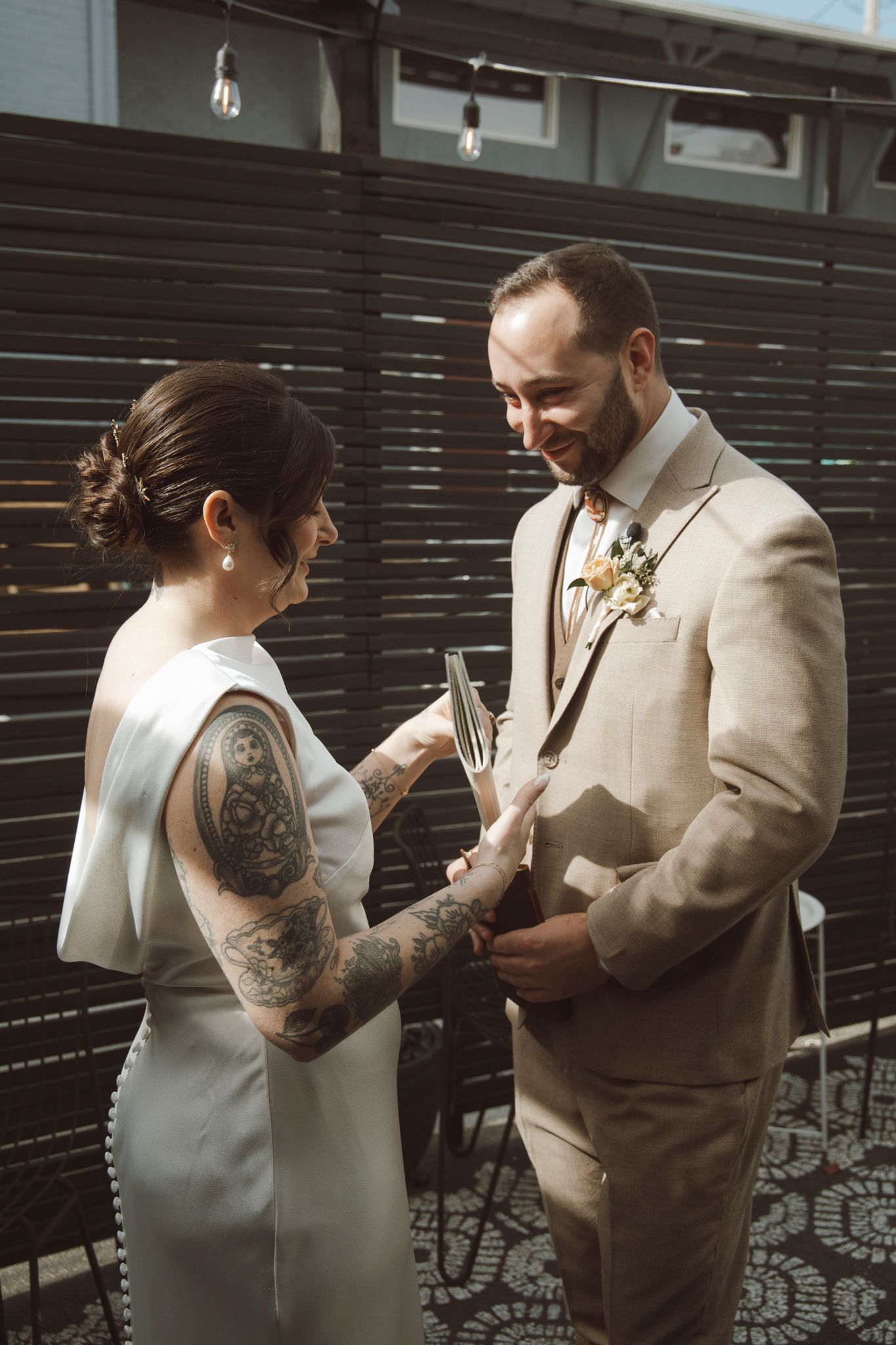A couple exchanges rings during their wedding ceremony in front of a dark wooden wall.