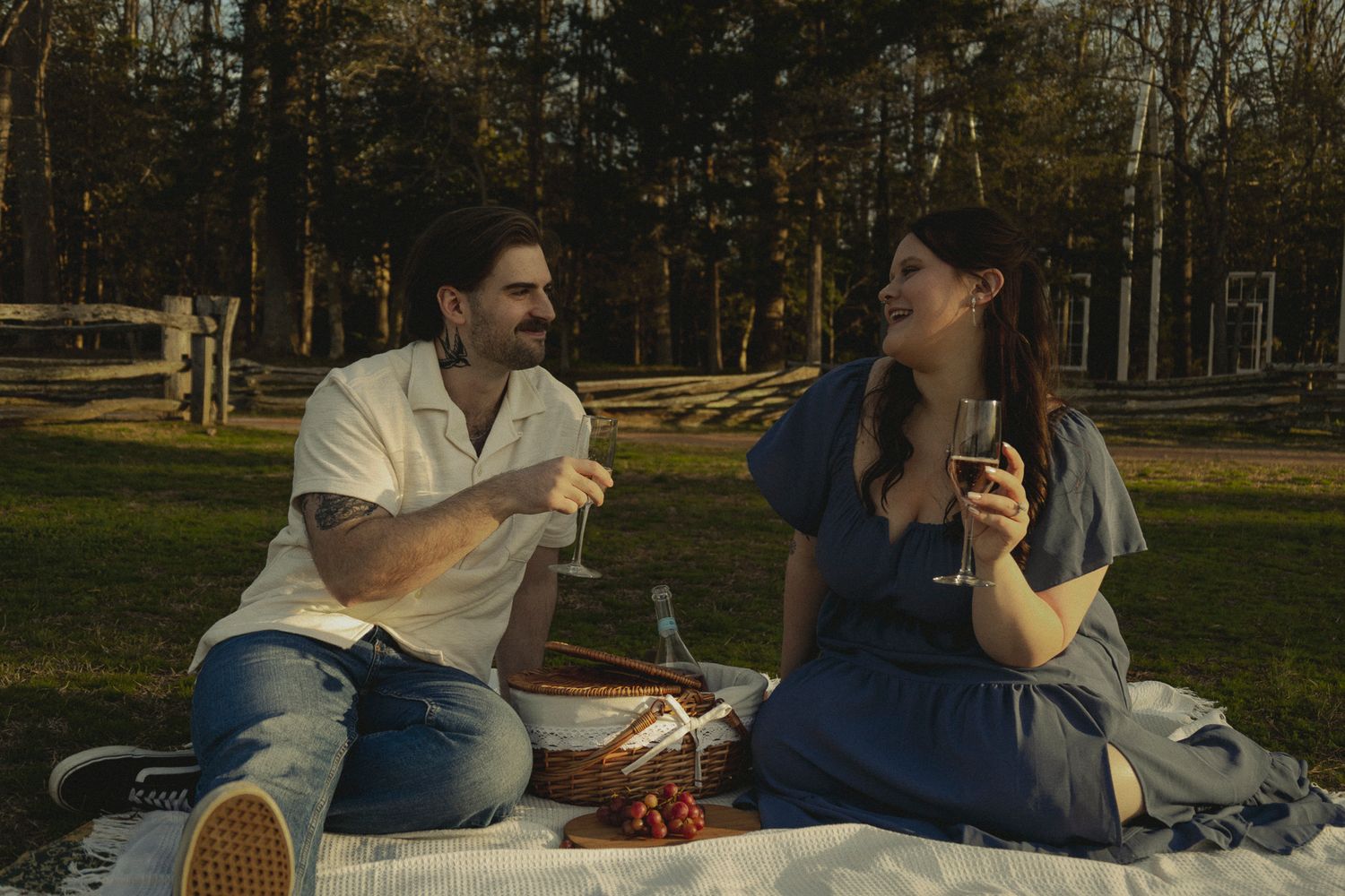 Couple enjoying a romantic outdoor picnic on a blanket, sharing wine and laughter in a sunny park setting.