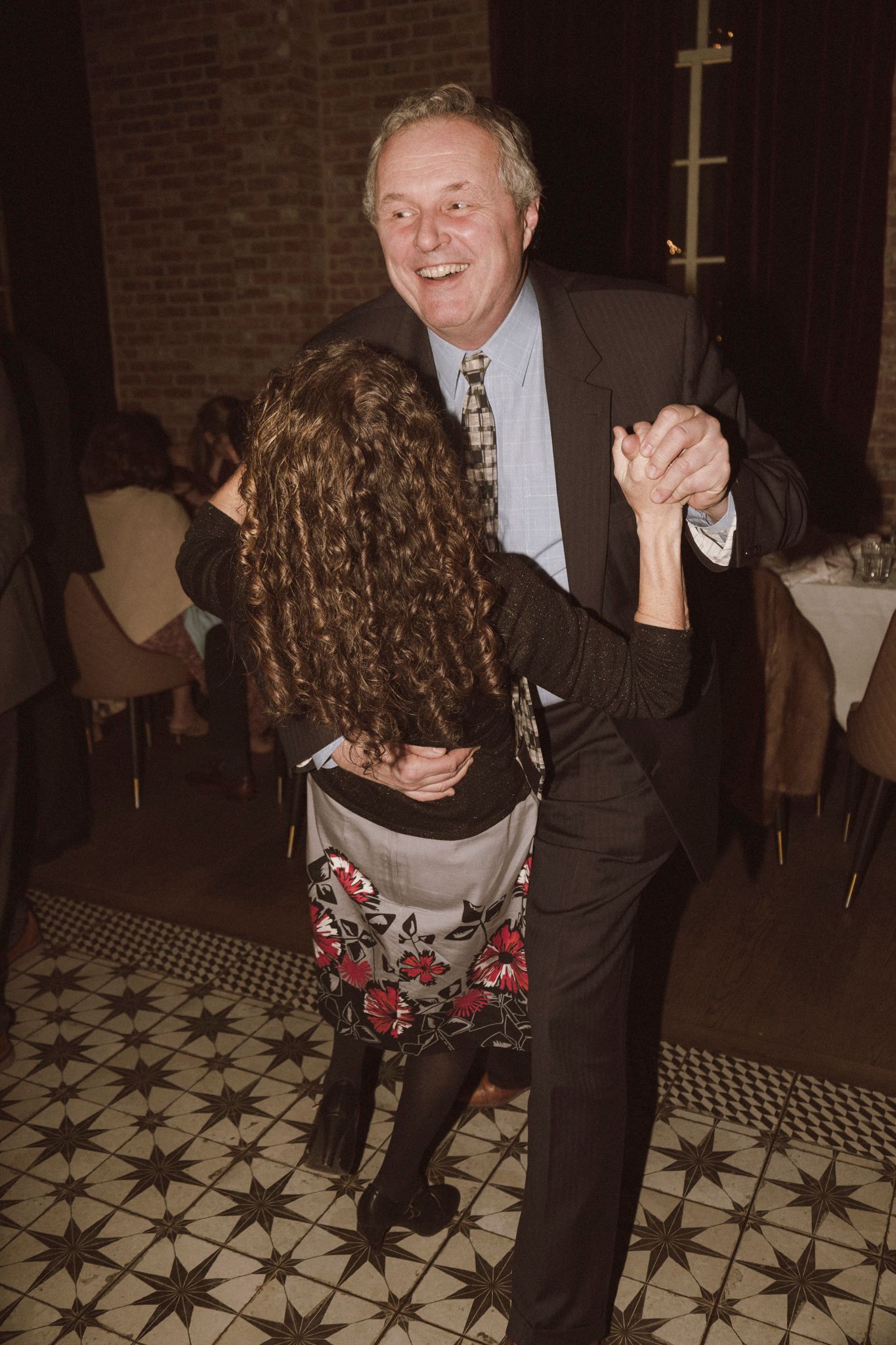 Smiling senior man dancing with curly-haired woman at a formal restaurant reception.