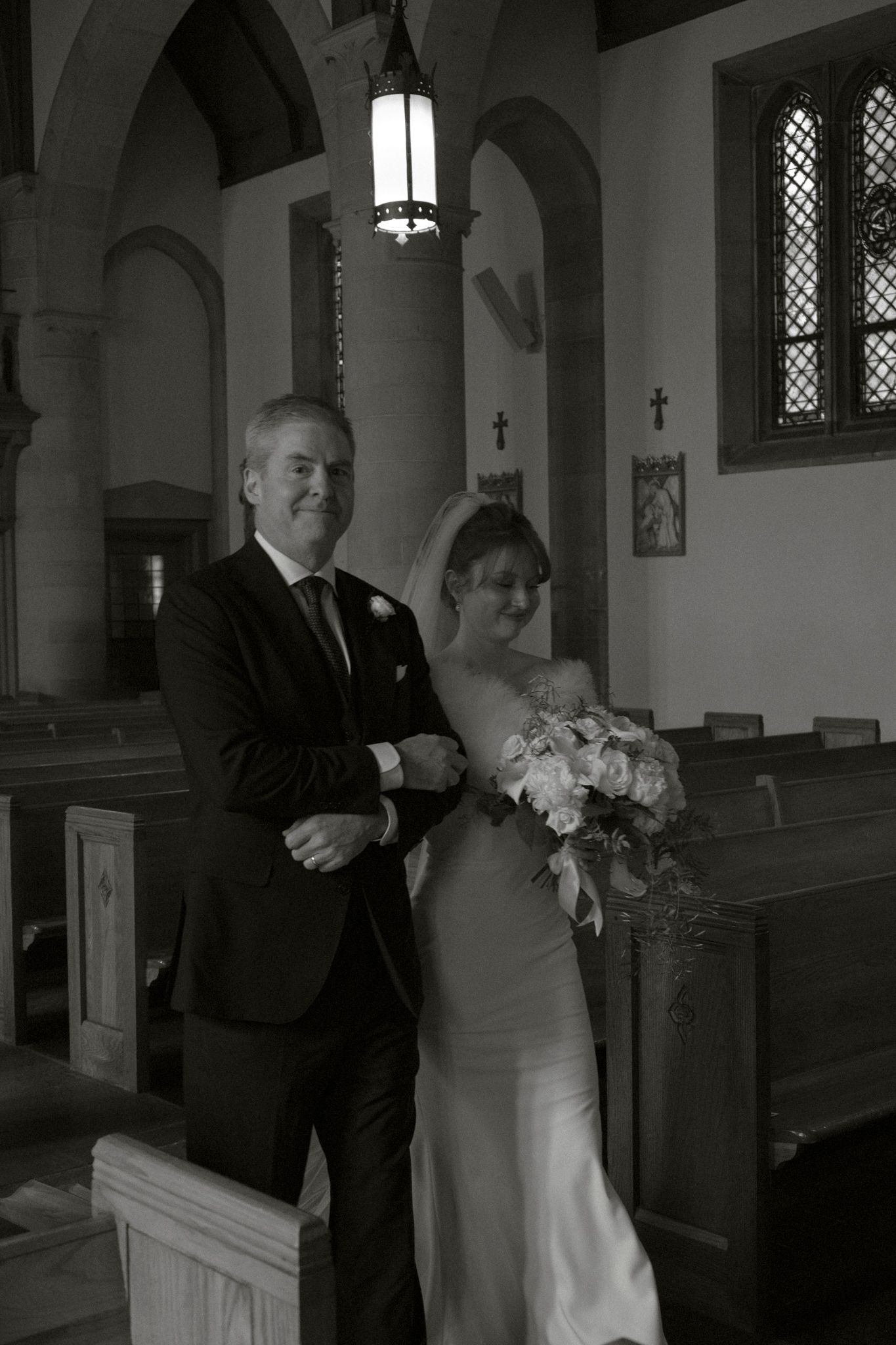 Black and white photo of a bride holding flowers standing with a man in a suit inside a church.