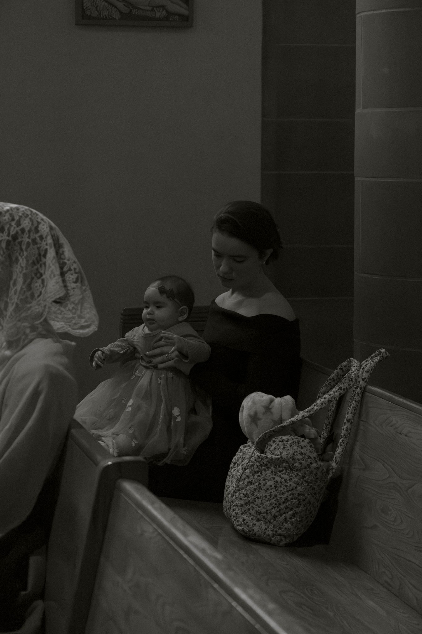 Black and white photo of mother with baby in church pew during wedding.