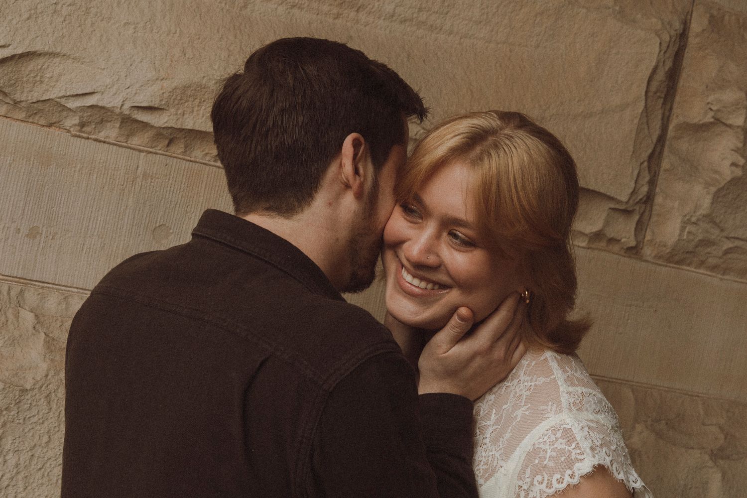 A romantic moment between a couple in vintage-style photography as they embrace against a textured wall.