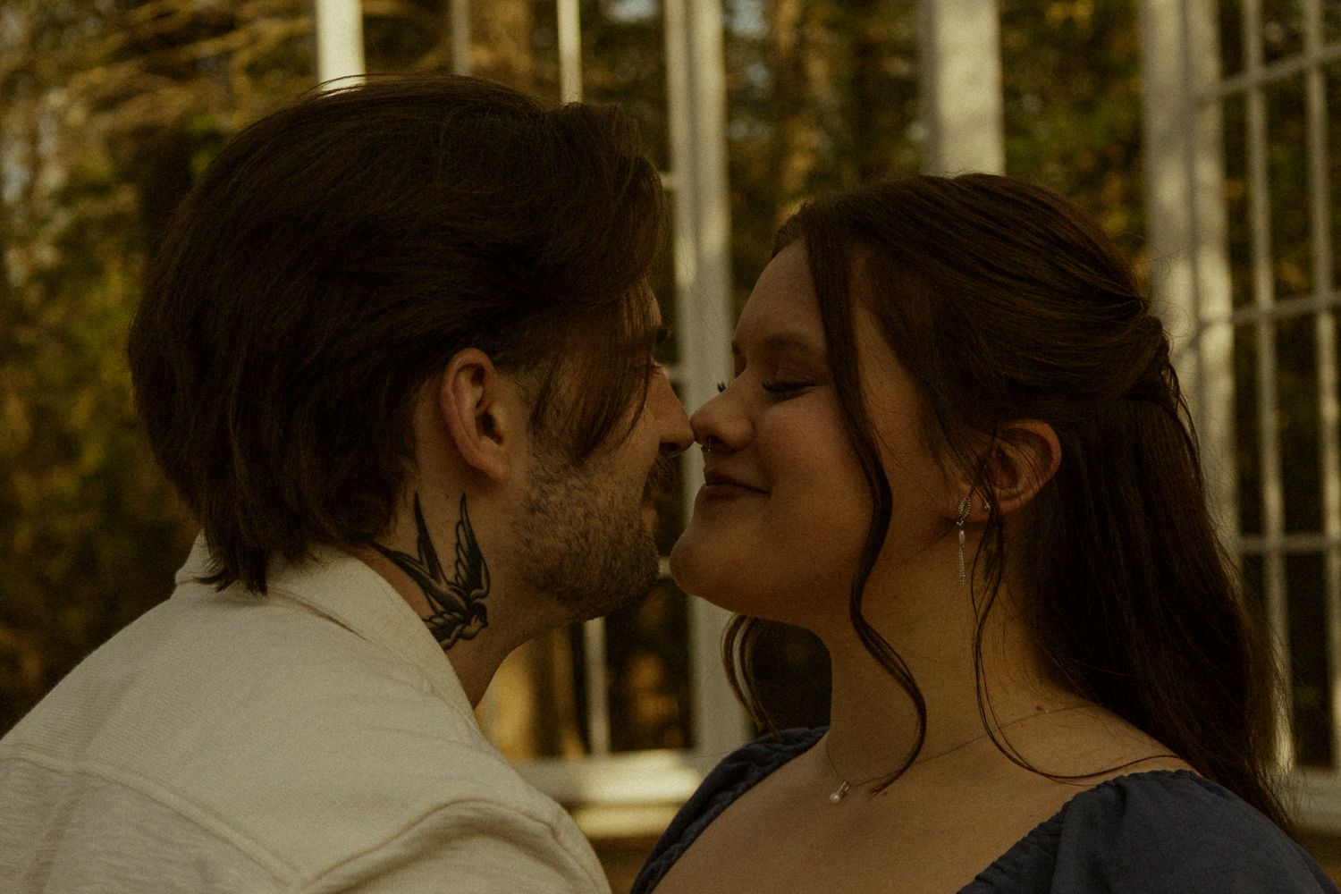 Romantic couple sharing an intimate moment, almost kissing outdoors near a greenhouse.