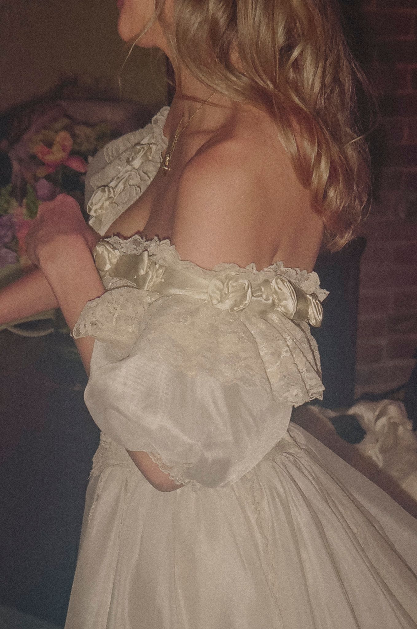 A dreamy vintage-style photo shows the back detail of a romantic white dress with delicate lace ruffles and gathered fabric.