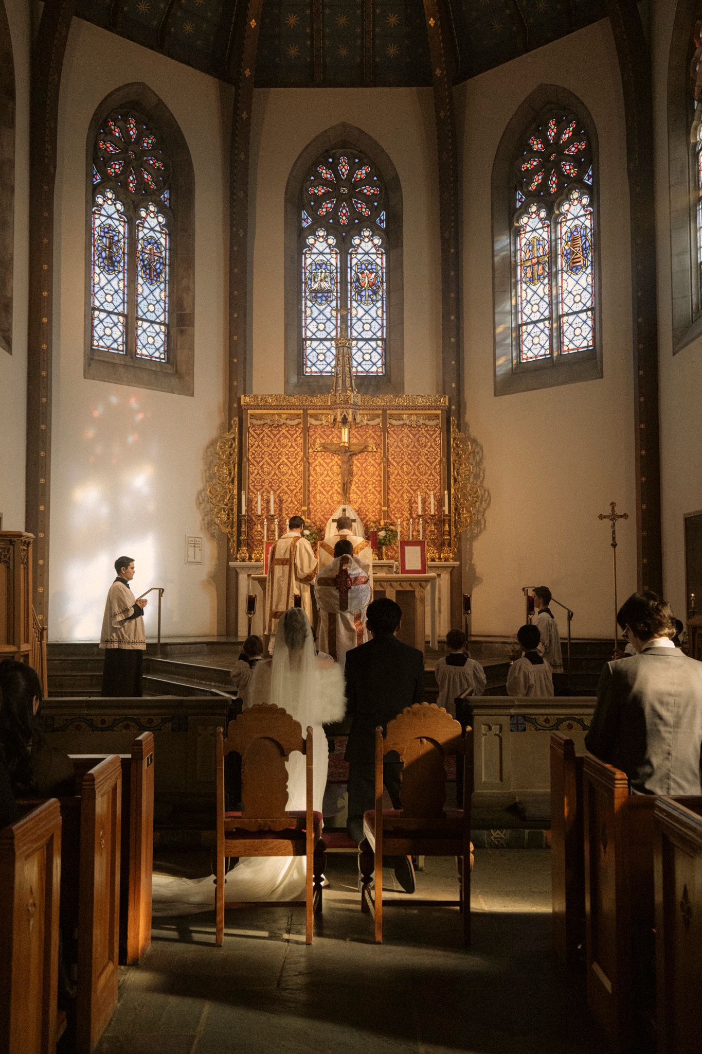 Bride and groom at ornate golden altar during church wedding ceremony with stained glass.
