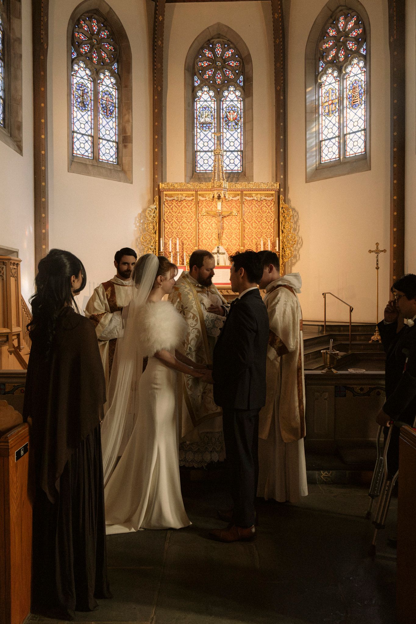 Bride and groom exchanging vows at the altar of a beautiful Catholic church with ornate golden reredos.