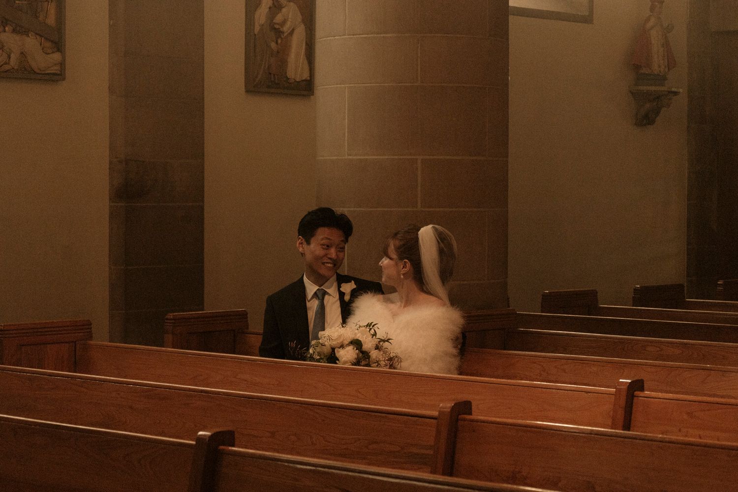 Bride and groom share a romantic moment seated in wooden church pews during their wedding ceremony.