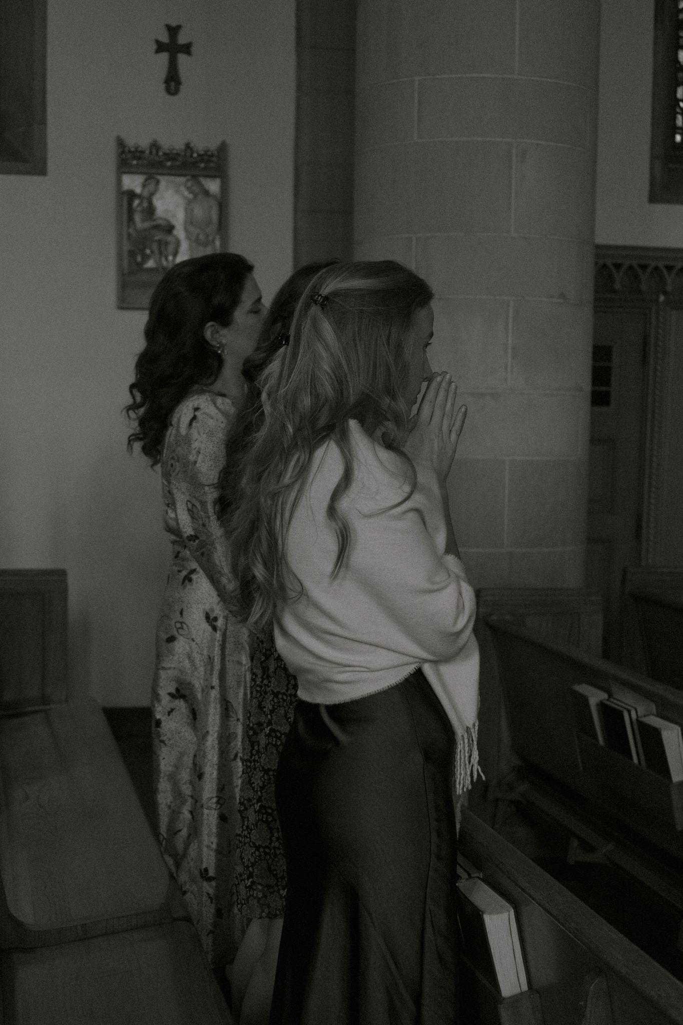 Black and white photo of two women praying with hands clasped in church.