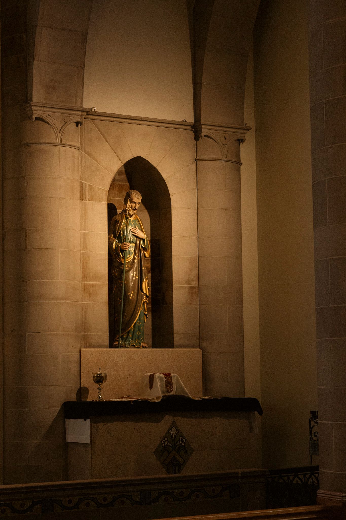 Religious statue in a stone niche above a small altar in a dimly lit Gothic church chapel.