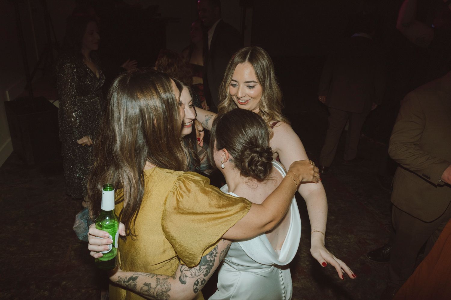 A group of people dancing and celebrating at a dimly lit party or reception venue.