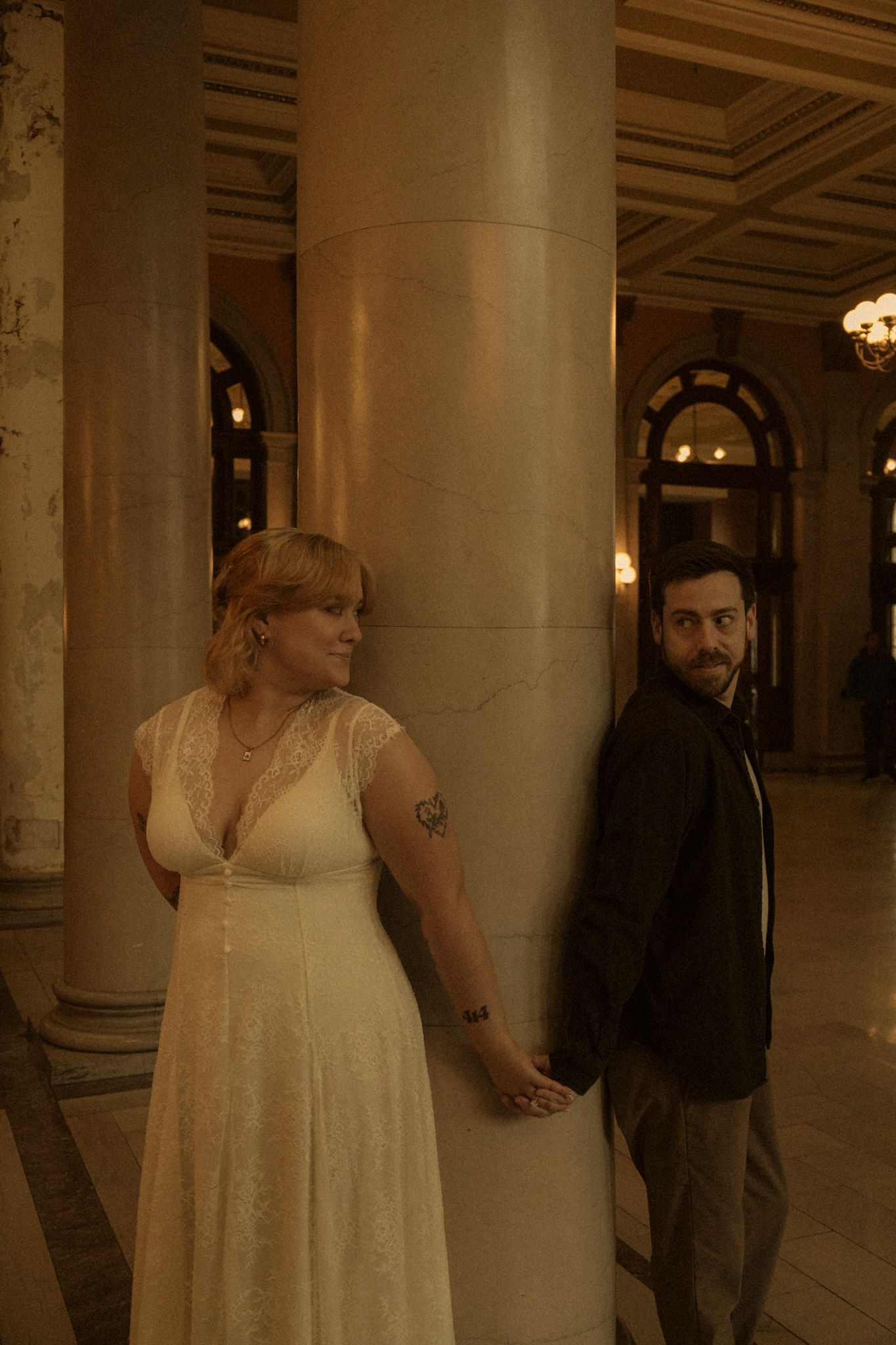 A couple poses between elegant columns in a grand indoor venue during their wedding photoshoot.