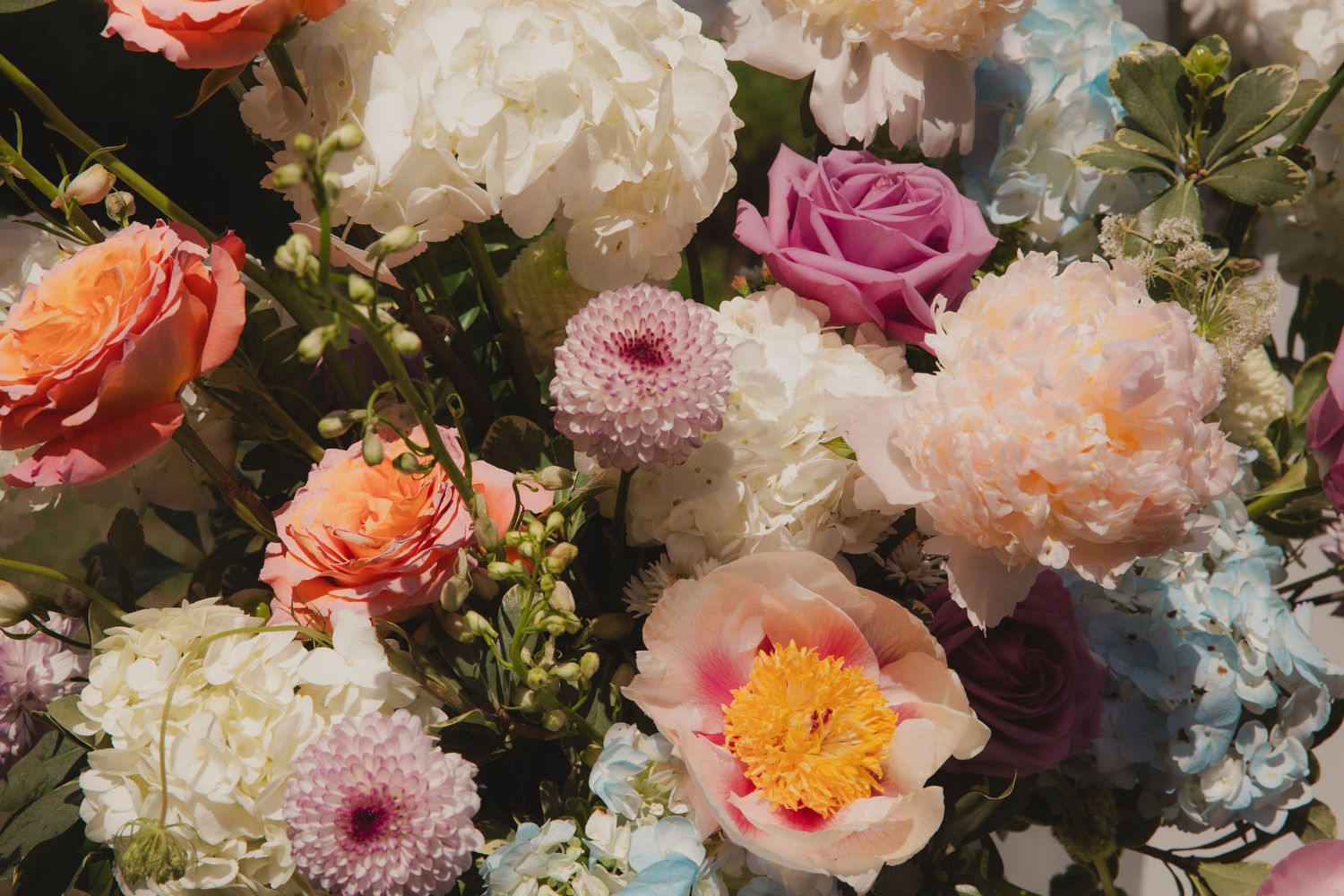 A lush floral arrangement featuring pink, orange, and white blooms with greenery in a romantic garden style composition.