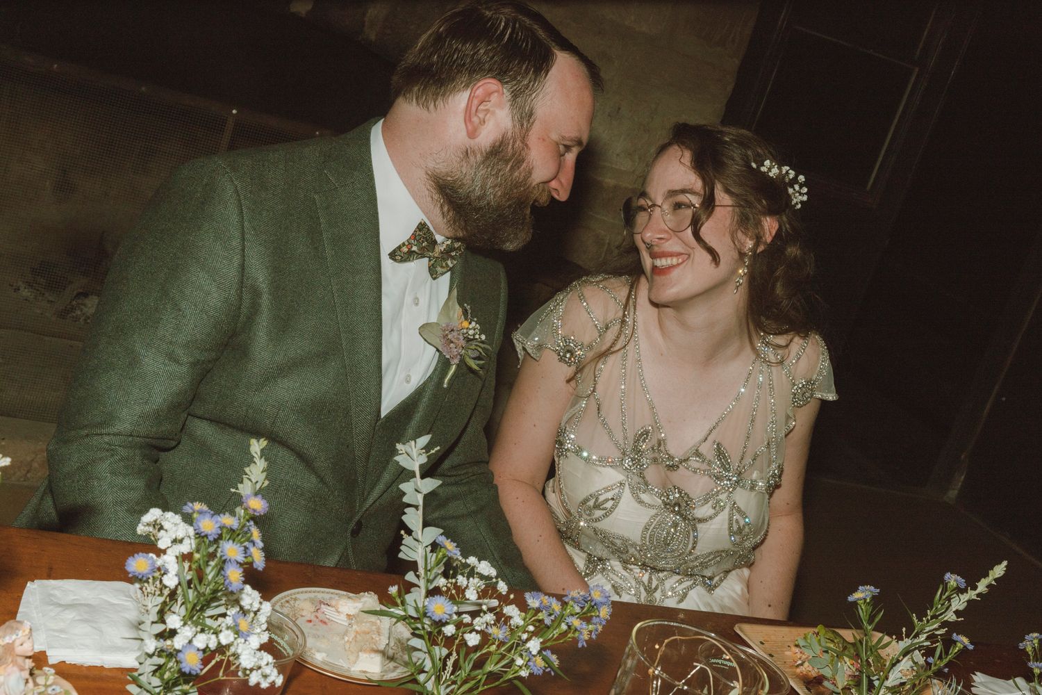 Wedding reception guests enjoy an intimate dinner gathering at a rustic table decorated with delicate white floral centerpieces.
