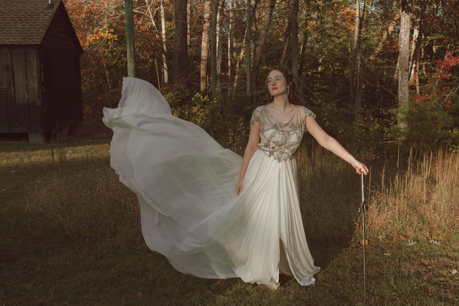 A flowing white wedding dress billows in the breeze during a golden hour autumn photoshoot in a wooded setting.