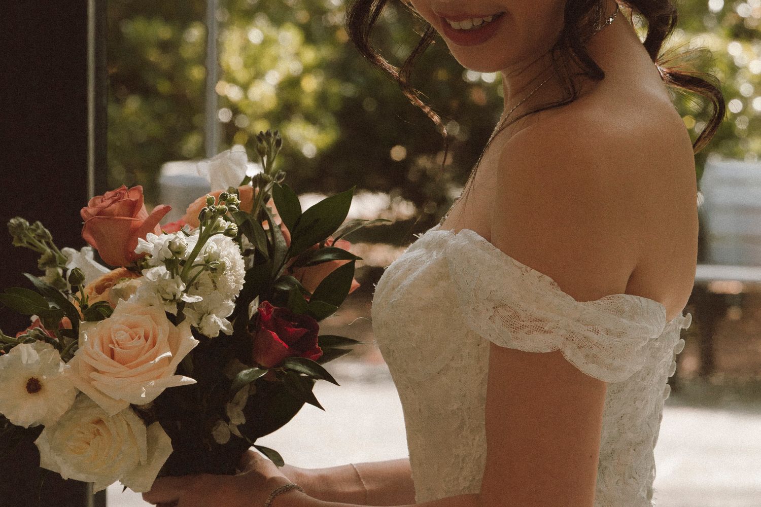 A wedding bouquet featuring blush pink and cream roses with cascading greenery and burgundy accents.