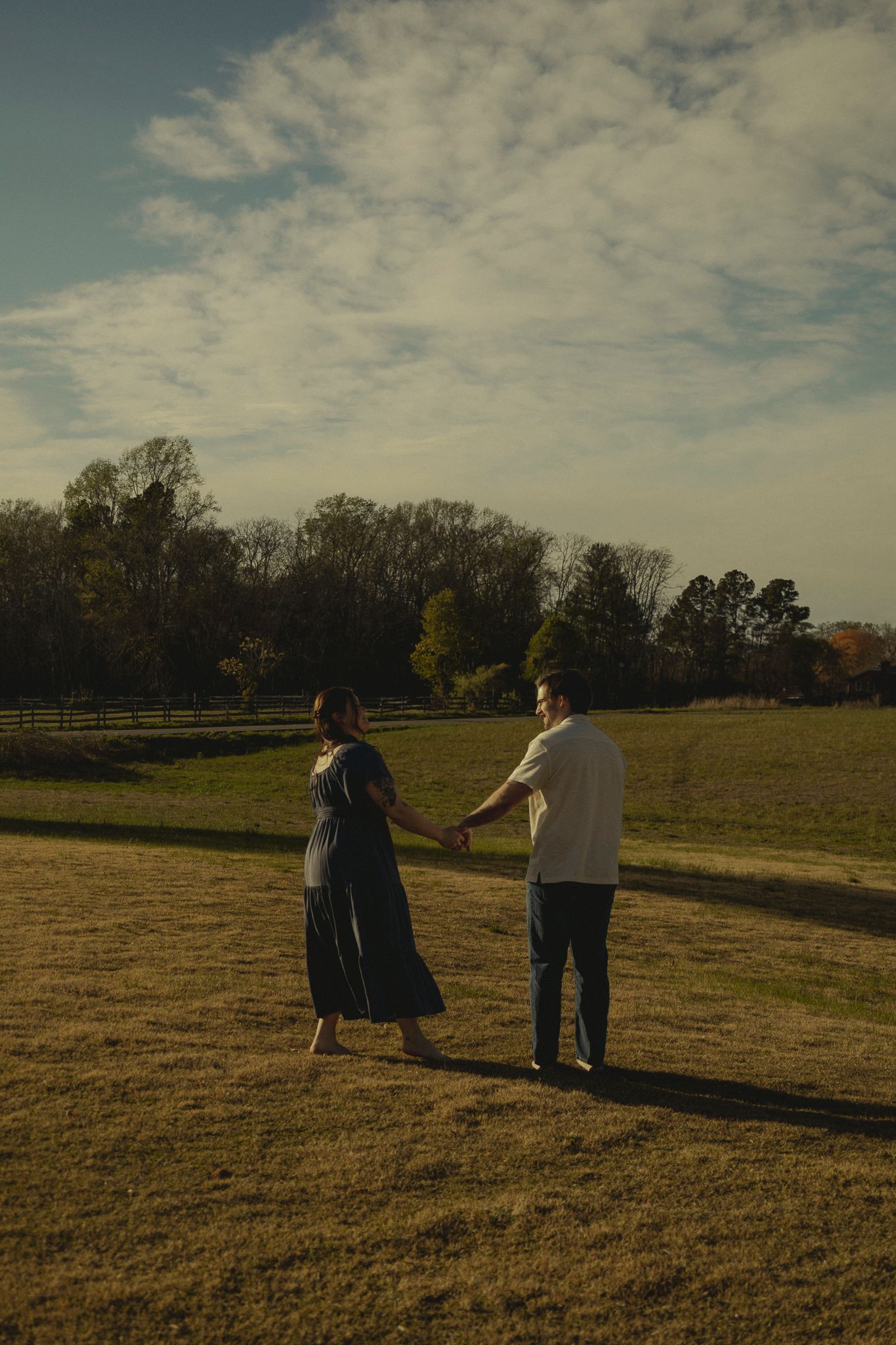 Couple holding hands while walking across a golden field at sunset.