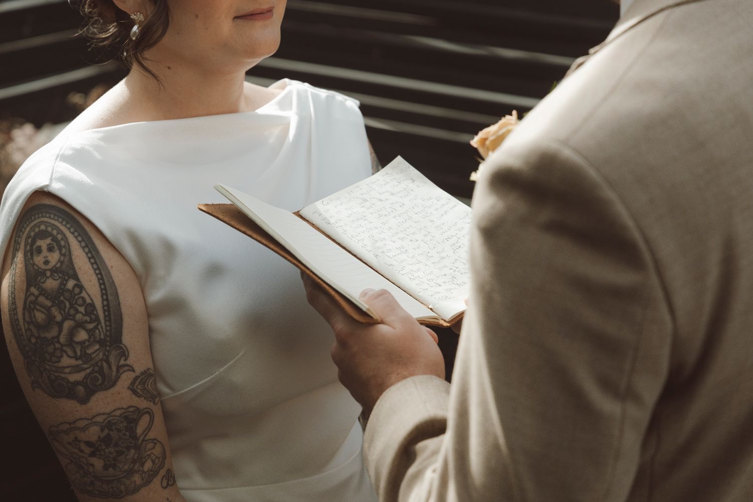 A close-up of a couple exchanging vows, with the bride wearing a white dress showing her tattoo sleeve.