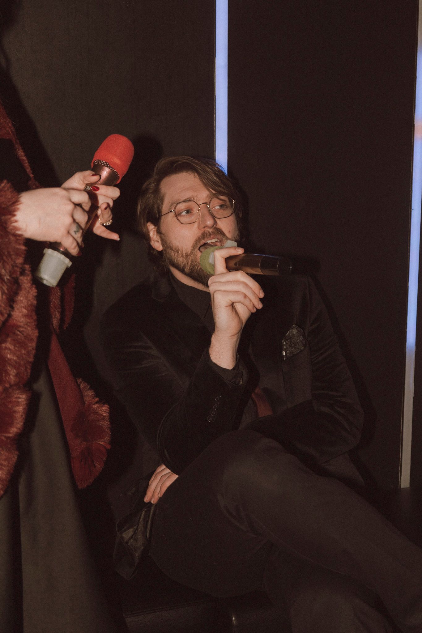 Person in black clothing performing on stage with expressive gestures and dramatic lighting.