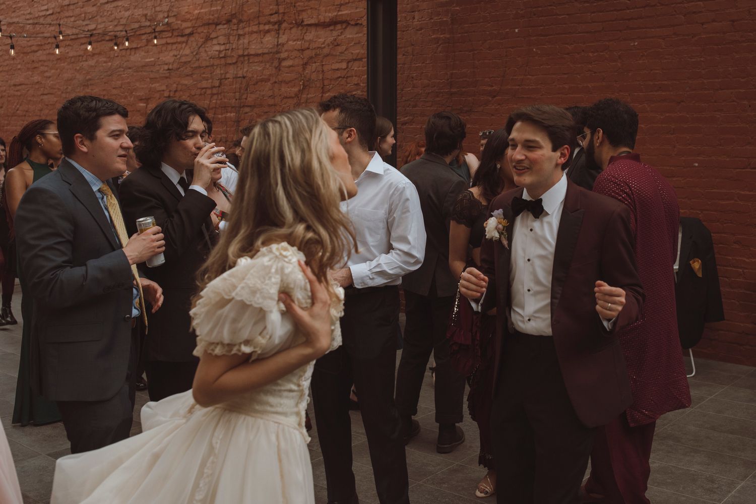 Wedding guests mingle and socialize during a reception in an elegant brick-walled venue space.