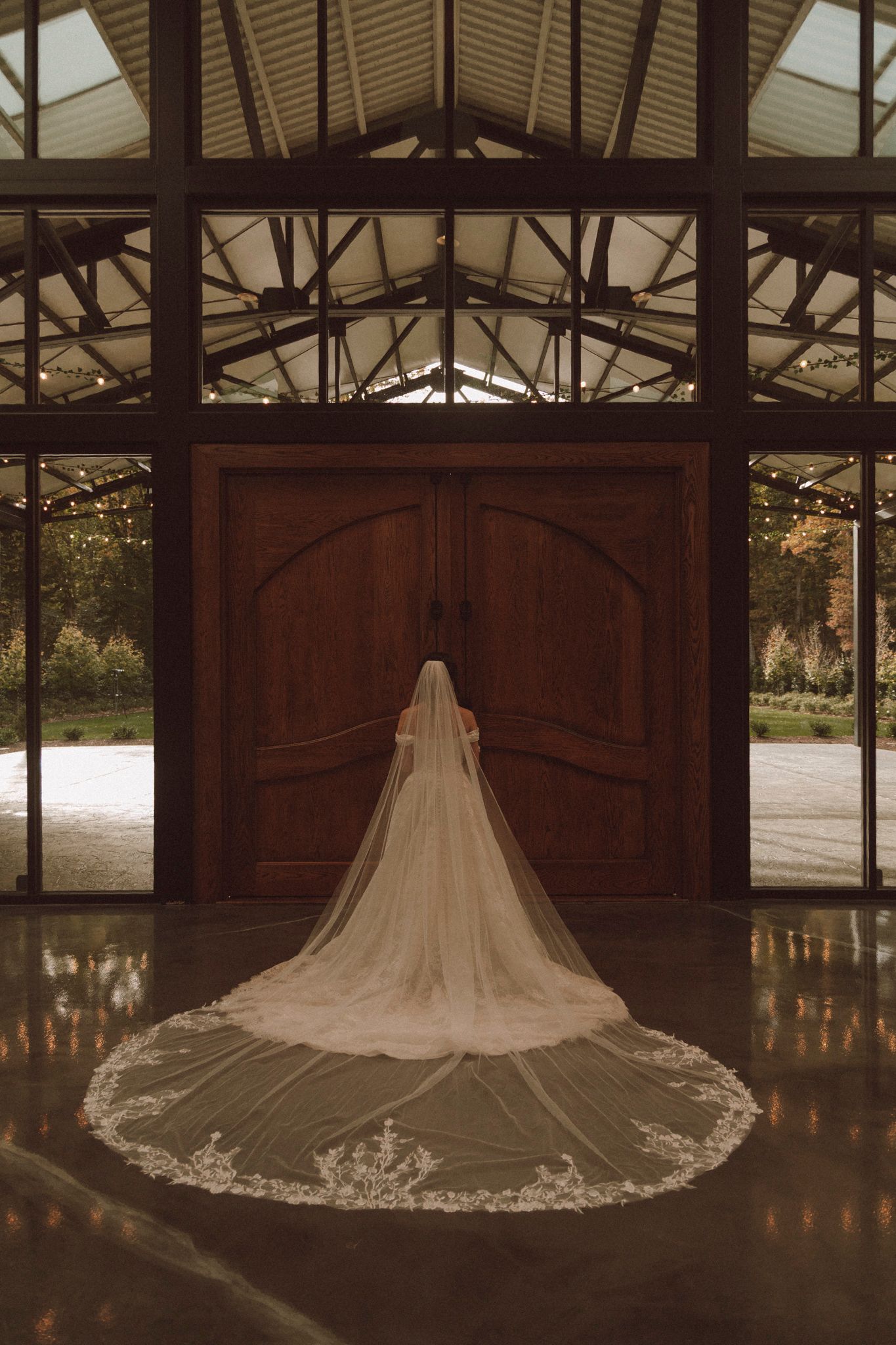 A stunning white wedding dress with a cathedral-length veil displayed in a rustic wooden barn setting with glowing candles.