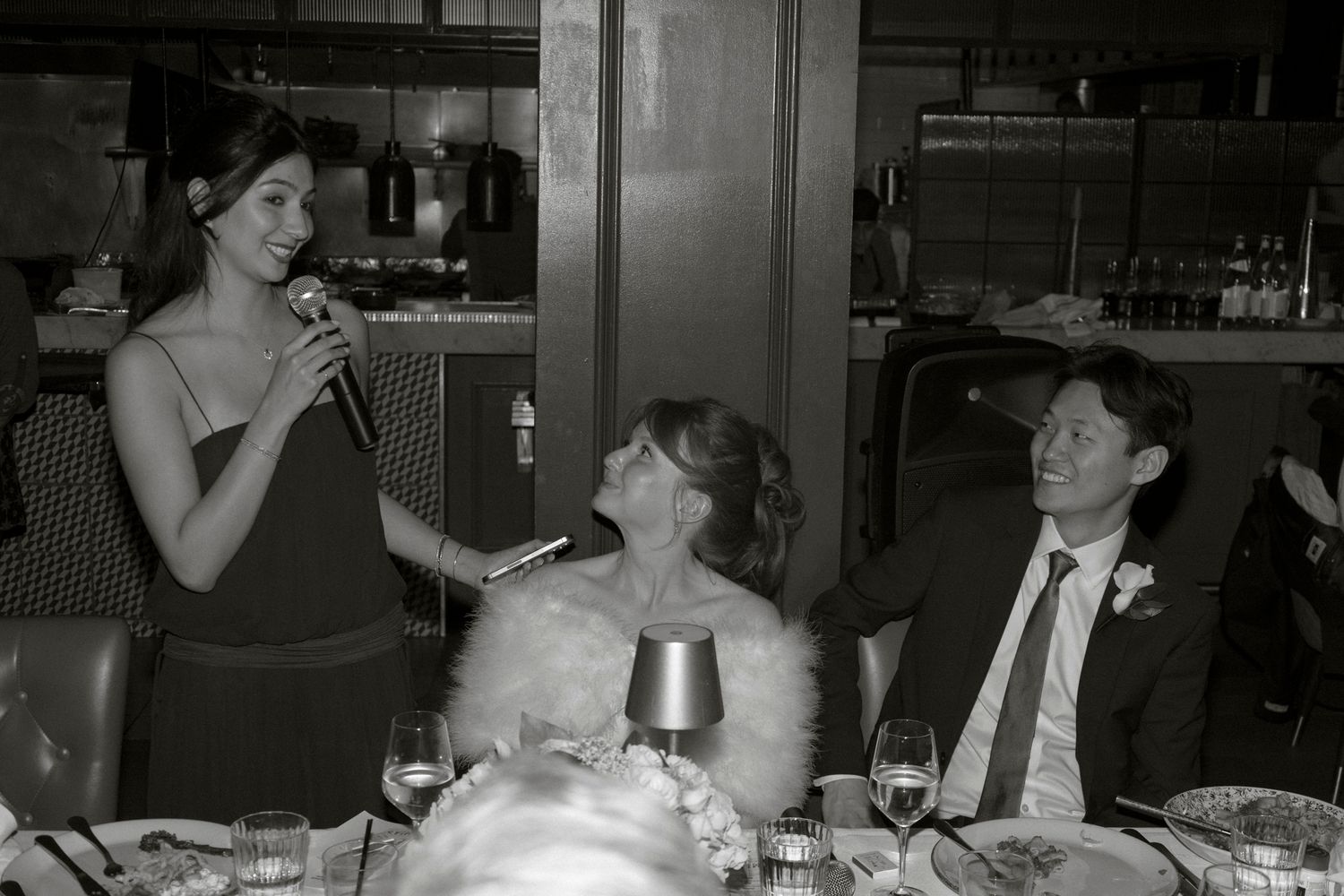 Black and white photo of bridesmaid giving toast speech at elegant wedding reception dinner.